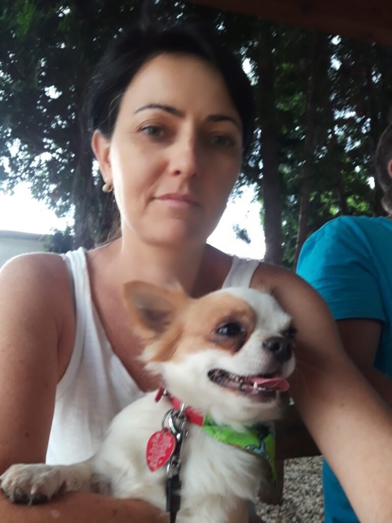 Woman with small dog outside on a bench.